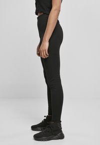 Zwarte leggings met een hoge tailleband en een gladde textuur, gecombineerd met zwarte hoge sneakers met veters en een gevoerde zool.
