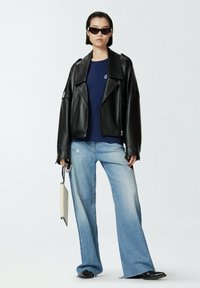 Crna kožna oversized jakna, tamnoplava majica, široke svijetloplave traperice. Dodaci uključuju crne sunčane naočale i malu bež torbicu.