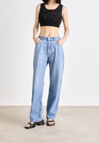 Débardeur noir court avec ourlet élastique, orné d'un petit logo rouge ; jean bleu clair taille haute avec jambe droite ; sandales à talons noires.