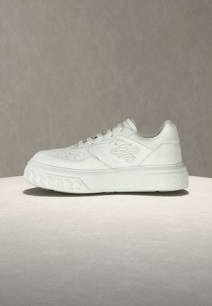 Baltas odinis sportinis batelis su plokščiu padu, perforuotu pirštu ir iškilusiu prekės ženklo akcentu šone, turintis tekstūruotus guminės medžiagos elementus.