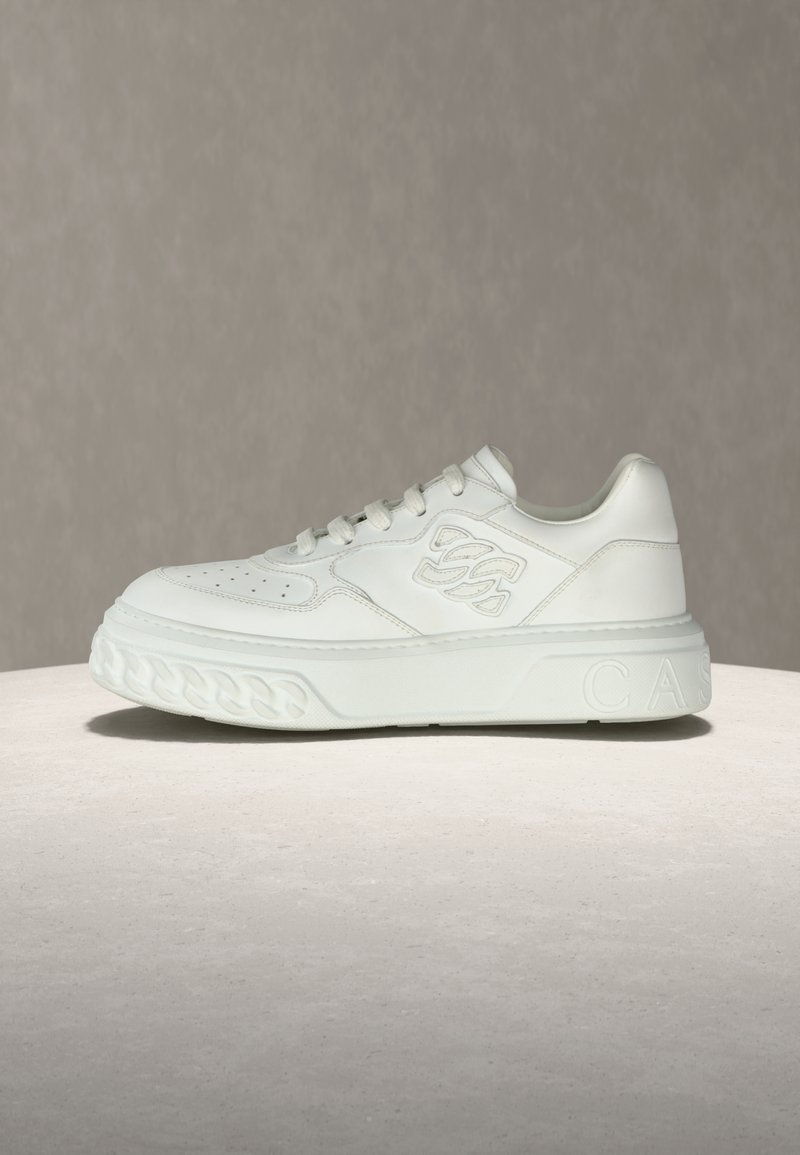 Baskets en cuir blanc avec une semelle plate, un bout perforé et un détail de marque en relief sur le côté, agrémentées d'accents en caoutchouc texturé.