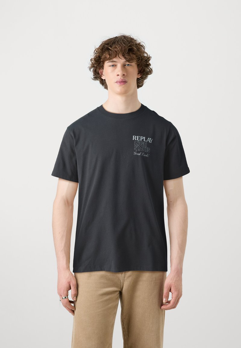 Svart bomullströja med rund halsringning och korta ärmar, med en tryckt grafik på vänster bröst som lyder "REPLAY HIGH STAKES Good Luck!"