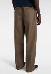Khaki wide-leg pants with a smooth texture, elastic waistband, and two back pockets. Features a small logo tag near the waistband.