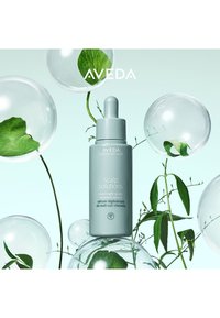 Sérum solutions cuir chevelu Aveda dans une bouteille vert clair avec un compte-gouttes. Entouré de bulles transparentes et de feuilles vertes sur un fond clair.