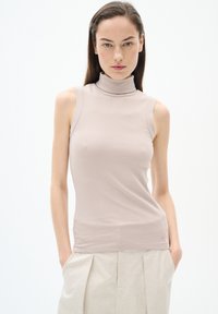Top smanicato beige a coste con un design aderente. Tessuto morbido e leggermente elastico. Abbinato a pantaloni plissettati di colore chiaro.