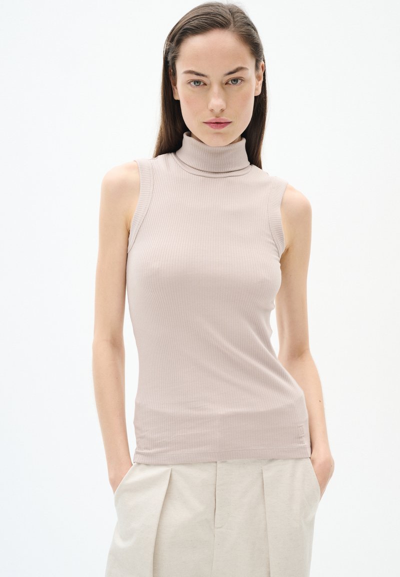 Top smanicato beige a coste con un design aderente. Tessuto morbido e leggermente elastico. Abbinato a pantaloni plissettati di colore chiaro.