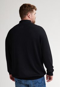 Schwarzer Baumwollpullover mit Kragen, langärmlig und in lockerer Passform. Texturiertes Material mit gerippten Bündchen.