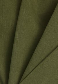 Tissu vert olive à la texture rugueuse, présentant des sections pliées et un tissage serré. La lumière se reflète subtilement à la surface.