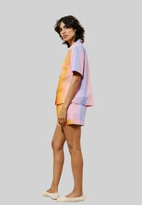 Kleurige twee-delige outfit met een kortemouwenshirt in oranje en roze tinten met een zak, gecombineerd met bijpassende shorts en gestructureerde schoenen.