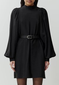 Zwarte jurk met pofmouwen en hoge halslijn, cinched in de taille met een zwarte riem, voorzien van een gladde textuur en een lengte tot de knie.