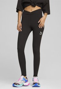 Schwarze Leggings mit einem V-förmigen Bund und Logodetails. Kombiniert mit bunten Sportschuhen, die eine Mischung aus rosa, blau und silbernen Akzenten aufweisen.