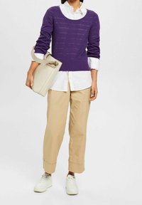 Pull en maille violette avec un col rond, chemise boutonnée blanche en dessous, pantalon beige et baskets blanches. Sac à main beige clair.