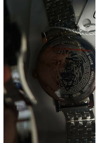 Metalen polshorloge met gegraveerd leeuwenkop en Grieks sleutelmotief op de achterkant, met details van roestvrij staal en saffierkristal.