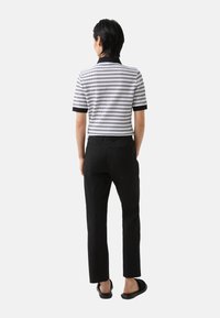 Polo �à manches courtes à rayures horizontales noires et blanches, associé à un pantalon noir et des sandales noires. Design simple et moderne.