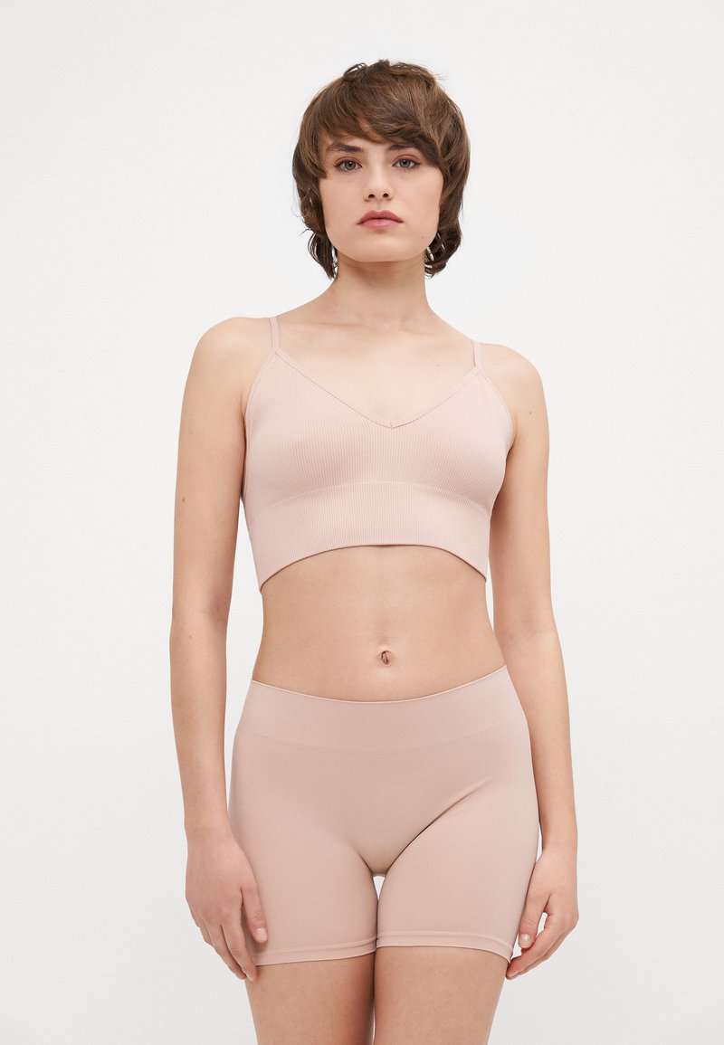 Ljusrosa ribbad bralette med tunna band och kort design, tillsammans med matchande släta, elastiska shorts som visar upp en sömlös look.