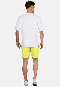 Camicetta bianca a maniche corte, vestibilità rilassata, abbinata a pantaloncini gialli vivaci. Completata con sneakers bianche, design semplice, senza motivi visibili.