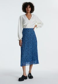 Weißes Blusenshirt mit Puffärmel; Rock mit blauem Blumendruck; schwarze, klobige Slipper; lockere Passform, leichtes Material.