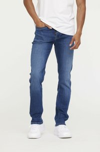 Jean en denim bleu moyen, coupe slim, avec un design classique à cinq poches et des détails de couture subtils, portés avec des baskets blanches.