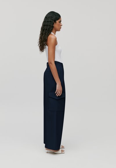 Marine blauwe wijde broek met een zijzak, gemaakt van soepele stof. Gemaakt om te dragen met een nauwsluitend wit tanktop, met een hoge taille en een op maat gemaakte uitstraling.