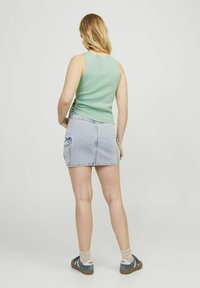 Mint zelena majica bez rukava, svijetloplava denim mini suknja s bočnim džepovima, uparena s bež čarapama i tirkiznim tenisicama, prikazuje ležeran izgled.