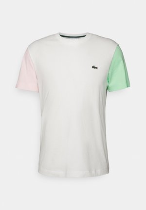 T-shirt blanc à manches courtes avec une manche gauche rose pâle, une manche droite vert menthe et un petit logo de crocodile vert sur la poitrine.