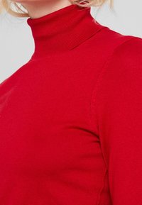 Czerwony sweter golfowy wykonany z prążkowanego materiału. Posiada długie rękawy oraz dopasowany krój, charakteryzuje się gładką fakturą i minimalnymi detalami szwów.