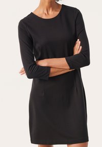 Robe noire avec un col rond, des manches trois-quarts, une coupe ajustée et des poches latérales, fabriquée en matière lisse et extensible.