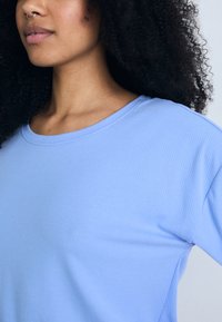 Ljusblå randig T-shirt med rund halsringning och korta ärmar. Tyget ser mjukt och texturerat ut, vilket ger en avslappnad look.