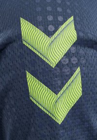 Le tissu en maille marine présente une surface texturée avec de grands pois sombres. Deux motifs en chevron chevauchants de couleur vert citron vif sont affichés de manière proéminente.