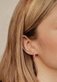 Pendientes de oro rosa con tres piedras preciosas transparentes, con un diseño curvado. Las piedras preciosas están dispuestas en un racimo.