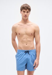 Ανοιχτό μπλε μαγιό σορτς με ελαστική μέση, μαύρο κορδόνι και λείο, ελαφρύ ύφασμα. Χωρίς σχέδια ή διακοσμητικά στοιχεία ορατά.