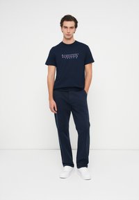 Navy katoenen T-shirt met een kleurrijk "tommy jeans" logo, gecombineerd met navy broek en witte sneakers. Eenvoudig, casual ontwerp.