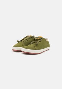 Grüne Segeltuch-Sneaker mit cremefarbenen Gummisohlen, ausgestattet mit einem Schnürdesign und orangefarbenen Akzenten in der Nähe der Zunge, glatte Textur.