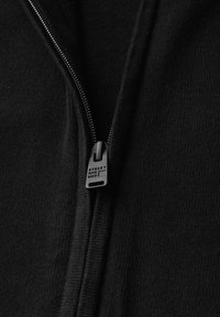 Černá mikina s kapucí na zip vyrobená z texturované tkaniny, s hladkým zipem a táhlem označeným "STREET ONE MEN." Jednoduchý a funkční design.