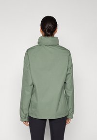 Lys grønn jakke med høy krage, elastiske mansjetter og løs passform, med en jevn, matt tekstur og minimalistisk design.
