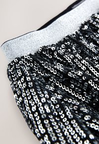 Tessuto nero con paillettes e fascia elastica argento lucida. Presenta file di paillettes rotonde e lucide che creano una superficie testurizzata.