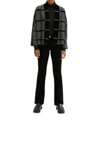 Grauer und schwarzer karierter Cardigan mit offenem Vorderteil und geripptem Kragen. Kombiniert mit einem schwarzen Rollkragenpullover und ausgestellten schwarzen Hosen, dazu schwarze Schuhe.