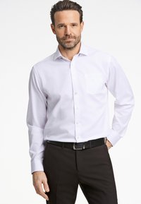 Wit langdijdskaphemd met een kraag en een enkele borstzak, gedragen met zwarte pantalon en een zwarte riem. Gladde textuur.