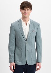 Lichtblauwe blazer van textuurstof, met twee voorzakken en een gedessineerde pochet. Draagt over een witte blouse met kraag.