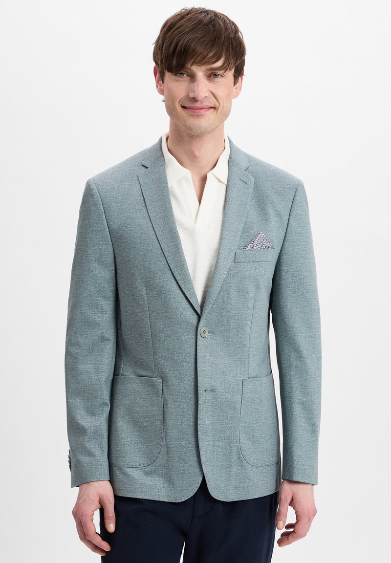 Lichtblauwe blazer van textuurstof, met twee voorzakken en een gedessineerde pochet. Draagt over een witte blouse met kraag.