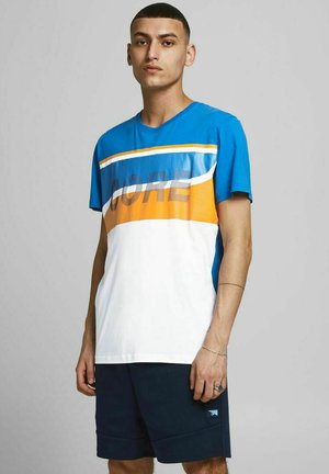 Maglietta blu e bianca con accenti arancioni e gialli, caratterizzata da una stampa in rete "CORE" e maniche corte. Indossata con pantaloni corti scuri.