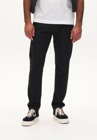 Dunkelgraue Jogginghosen aus weichem Material, mit schmal zulaufendem Beinin, elastischem Bund und Seitentaschen, kombiniert mit schwarzen Sneakers.