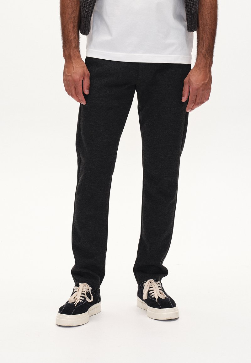 Dunkelgraue Jogginghosen aus weichem Material, mit schmal zulaufendem Beinin, elastischem Bund und Seitentaschen, kombiniert mit schwarzen Sneakers.