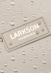 Textúrált anyagú táska világos bézs színben, vízcseppekkel. Egy téglalap alakú címke dombornyomott "LARKSON HAMBURG" felirattal fehér színben.