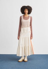 Cream-colored tiered maxi skirt with orange side stripes, worn with a fitted brown long-sleeve top and beige sneakers. Flat textured fabric.