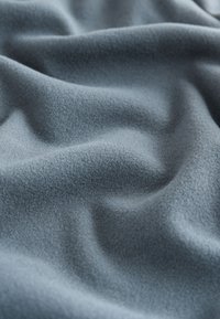 Weicher, hellblauer Stoff mit dezenten Falten und einer glatten, leicht strukturierten Oberfläche.