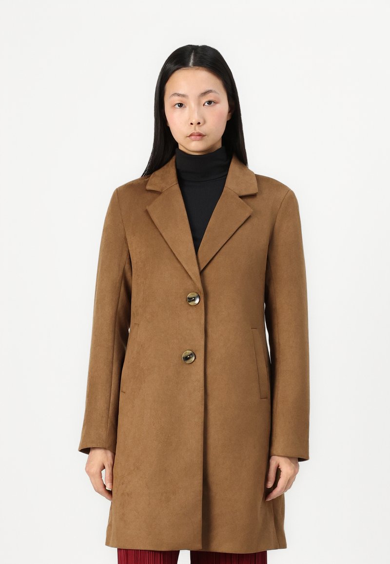 Brun, knappet frakk med en teksturert finish, store slag og sidelommer. Båret over en svart turtleneck, vist på en modell.