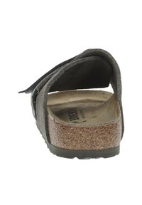 Vue arrière d'une sandale en daim marron avec une semelle en liège, une sangle réglable et un dessus texturé. Design plat adapté pour une tenue décontractée.