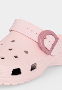Ροζ ανοιχτό Crocs με οπές αερισμού και πιο σκούρα ροζ ρυθμιζόμενη αγκράφα με λουράκι σε λευκό φόντο.