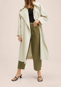 Jasno beżowy długi płaszcz z szerokim kołnierzem, w połączeniu z oliwkowymi spodniami. Noszony z czarną bluzką i czarnymi sandałami na paski.